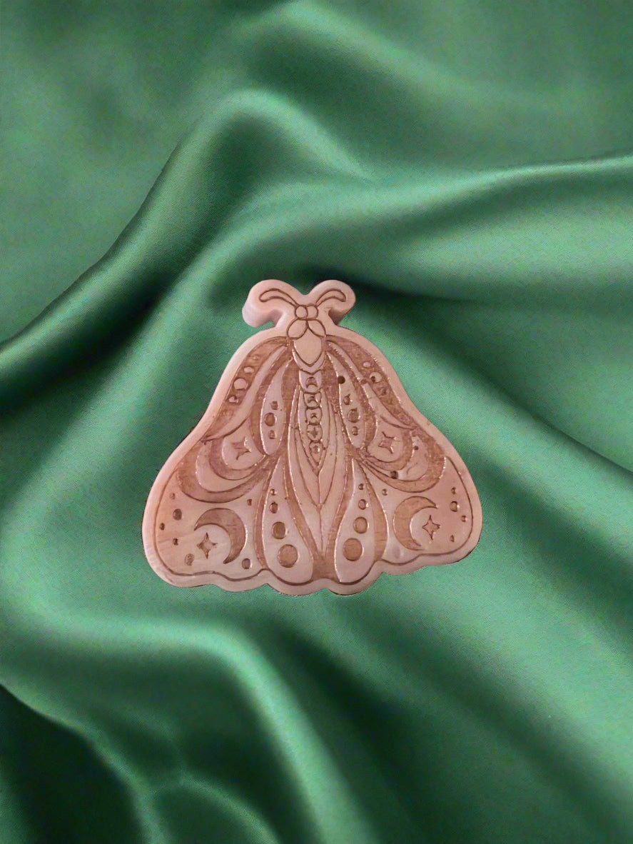 A Luna Moth wax melt with intricate patterns, placed on a green textured surface.