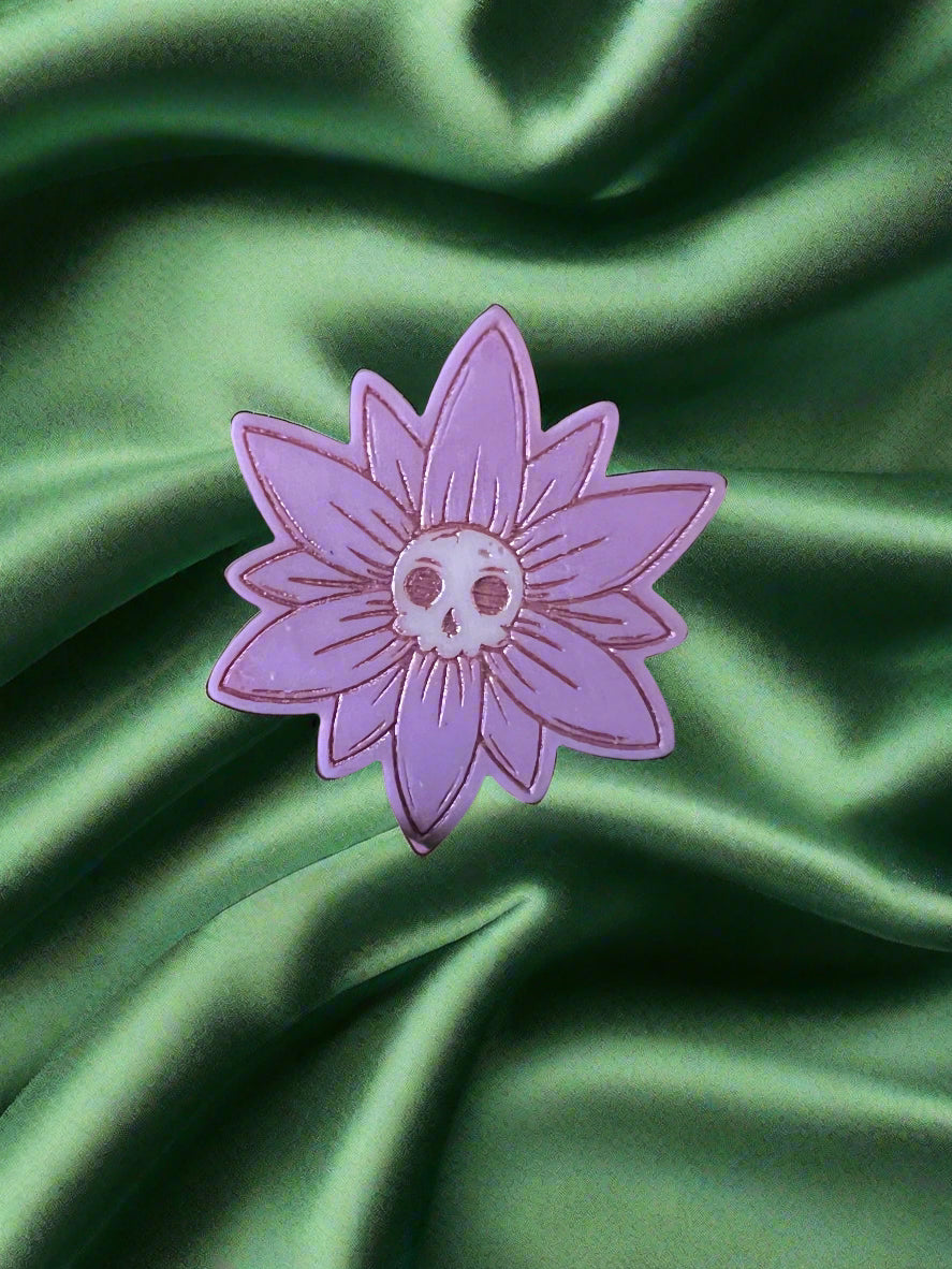 A white wax melt in the shape of a flower with a skull design at the center, placed on a green fabric surface.