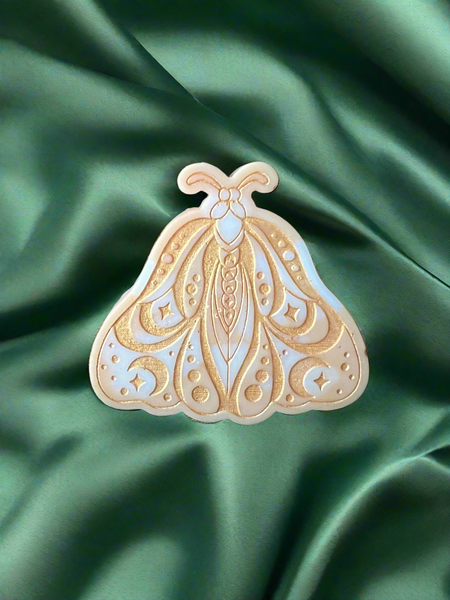 A Luna Moth wax melt with intricate patterns, placed on a green textured surface.
