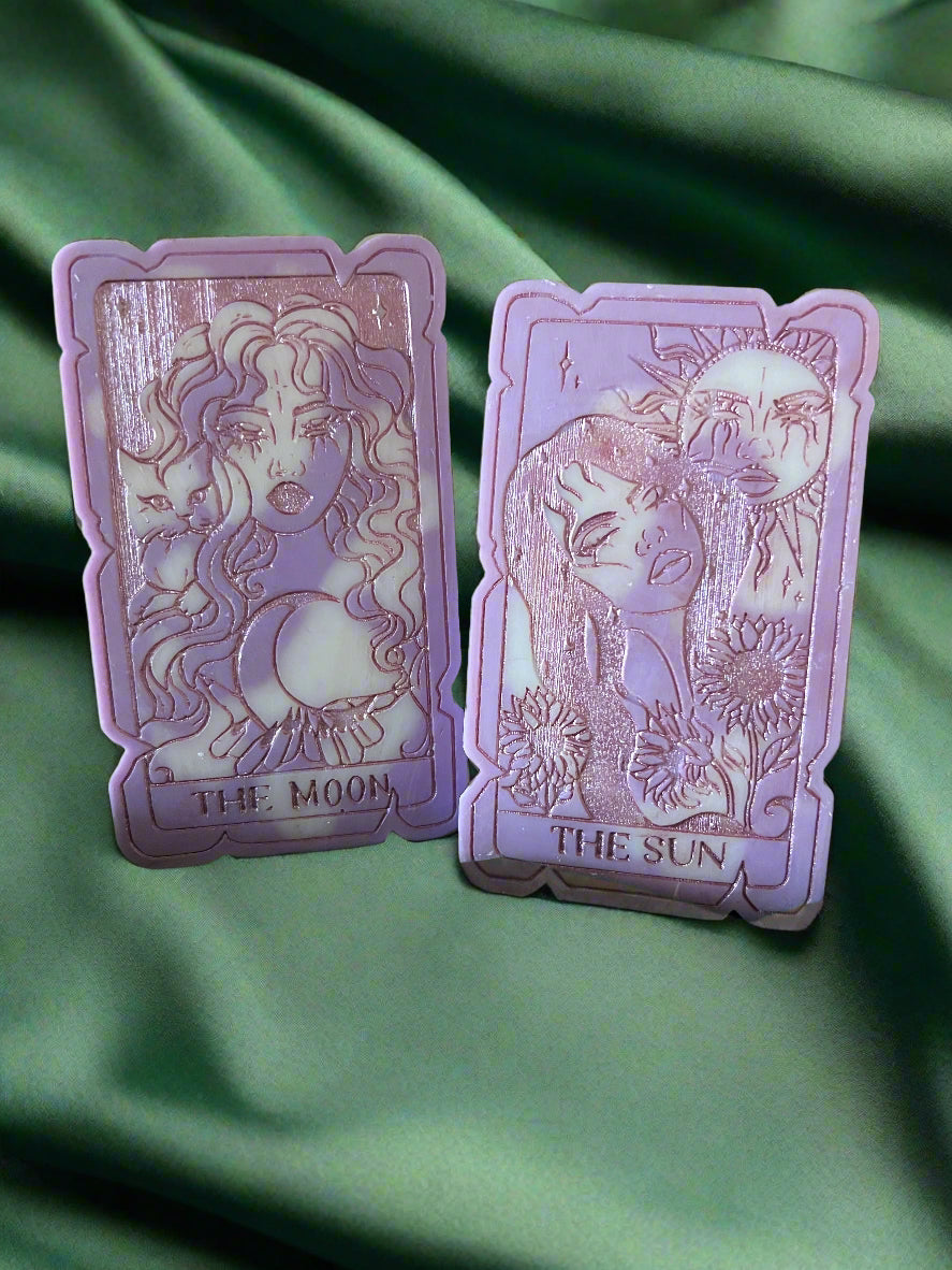 Two tarot card-shaped wax melts, one labeled 'THE SUN' and the other 'THE MOON', placed on a green fabric surface.