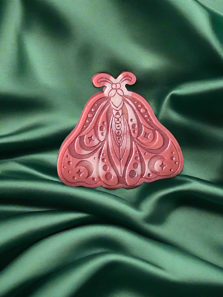 A Luna Moth wax melt with intricate patterns, placed on a green textured surface.
