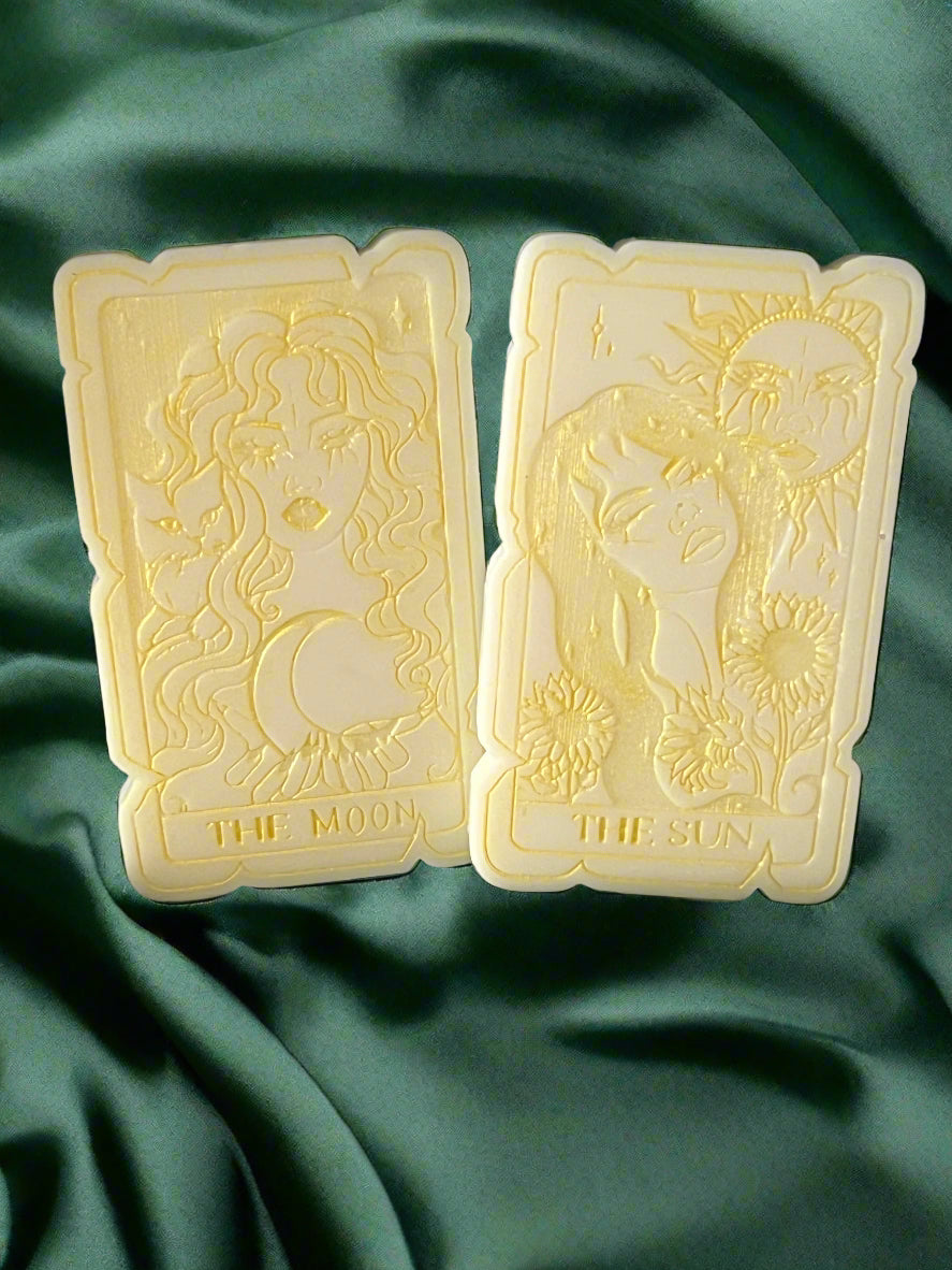 Two tarot card-shaped wax melts, one labeled 'THE SUN' and the other 'THE MOON', placed on a green fabric surface.