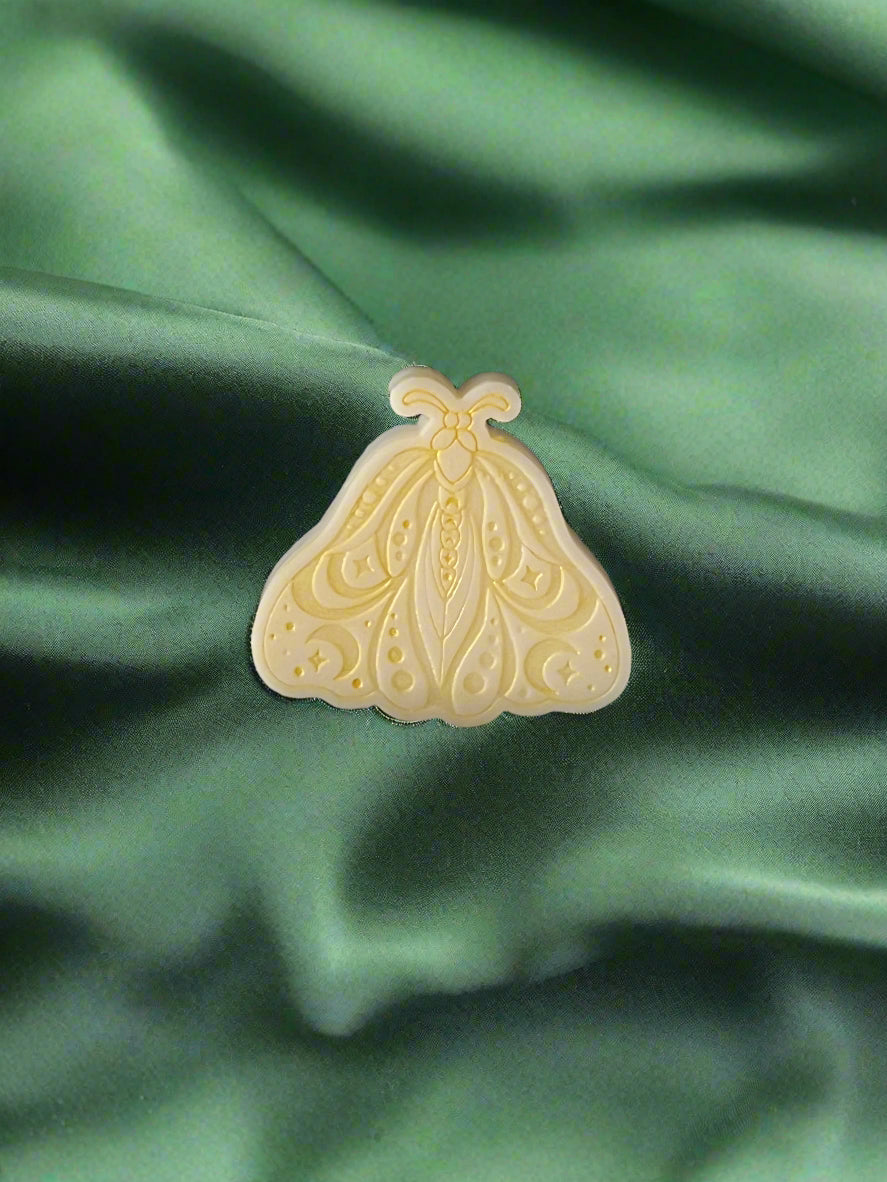 A Luna Moth wax melt with intricate patterns, placed on a green textured surface.
