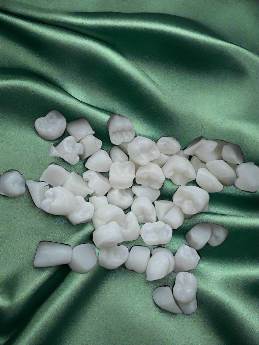 A collection of white wax melts shaped like teeth, placed on a dark green fabric surface.