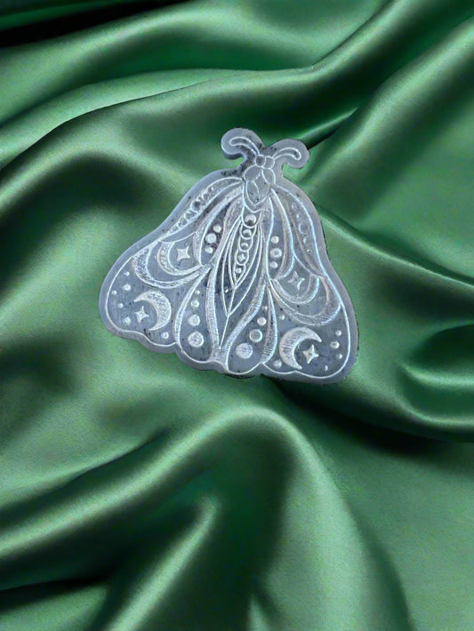 A Luna Moth wax melt with intricate patterns, placed on a green textured surface.