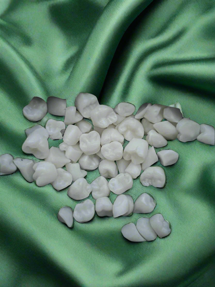 A collection of white wax melts shaped like teeth, placed on a dark green fabric surface.
