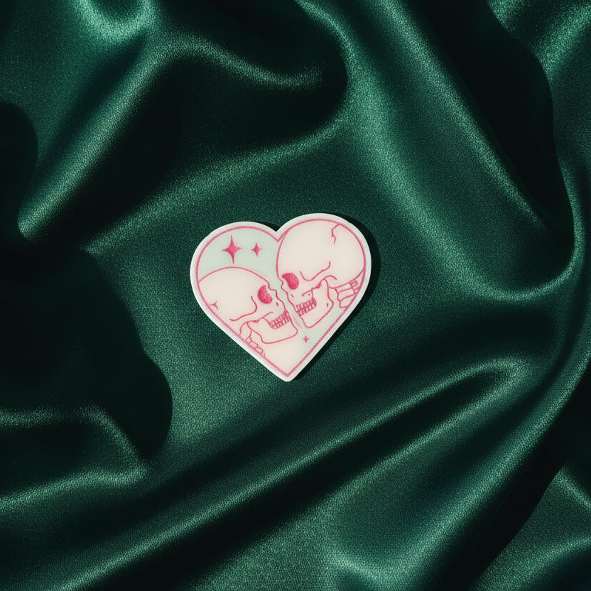 Heart-shaped pin with skull design on green satin fabric