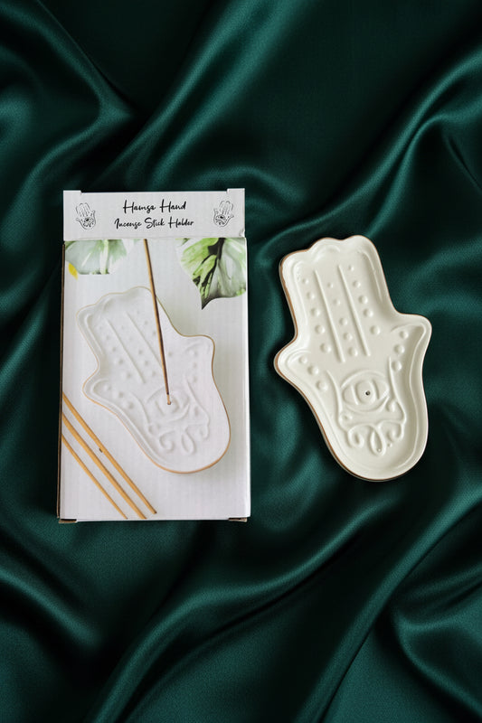 White ceramic hamsa-shaped tray on a green fabric background