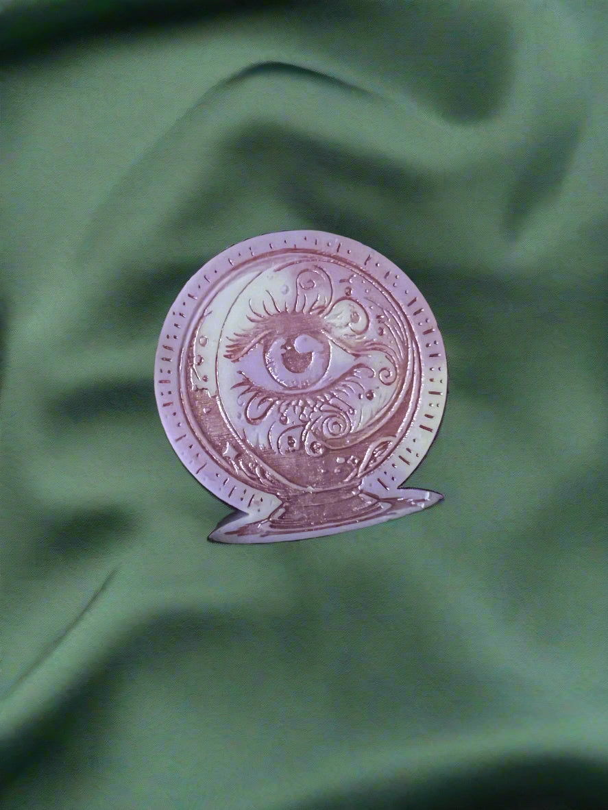 A silver-colored crystal ball wax melt with intricate designs, placed on a green textured surface.