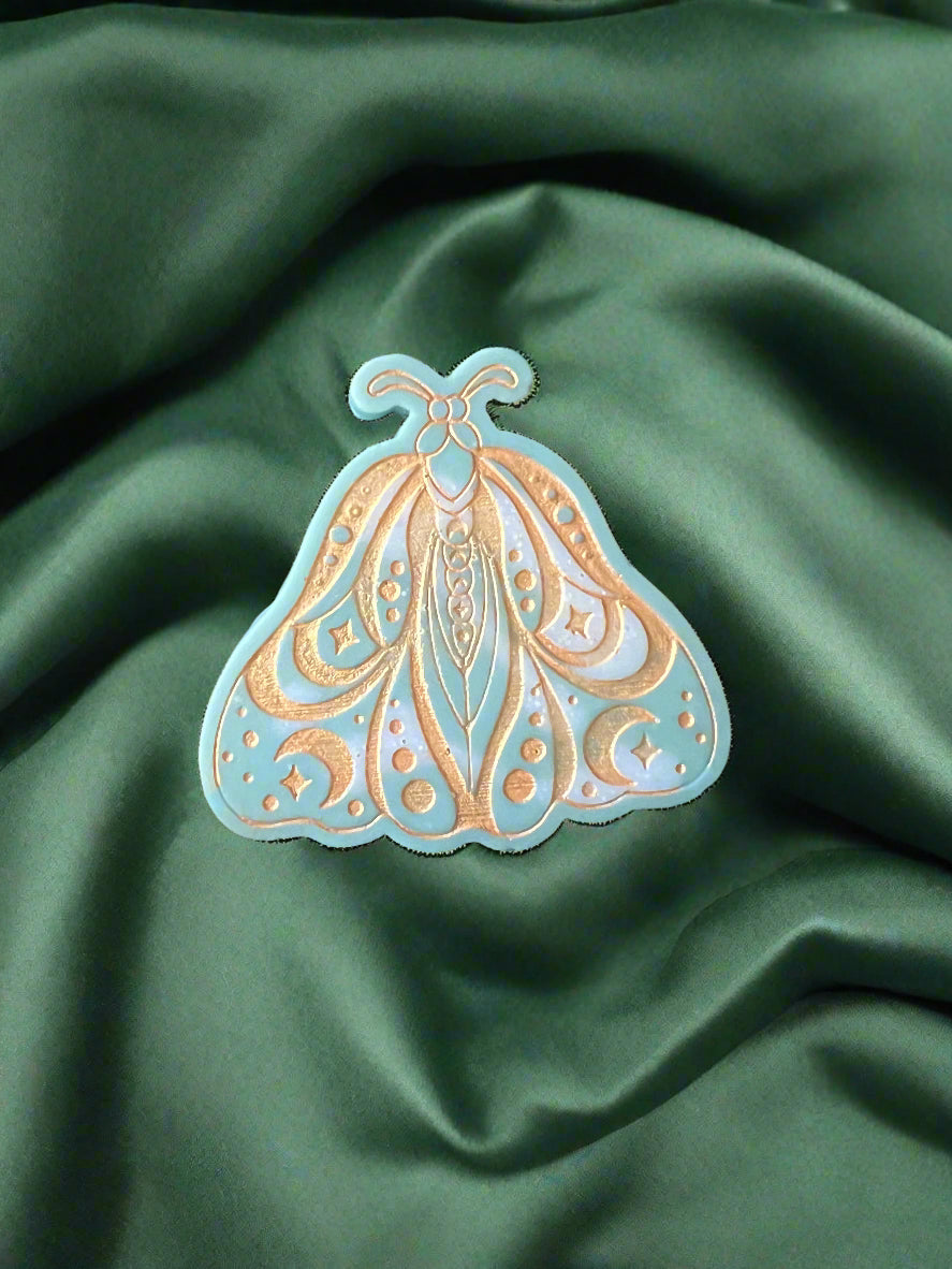 A Luna Moth wax melt with intricate patterns, placed on a green textured surface.