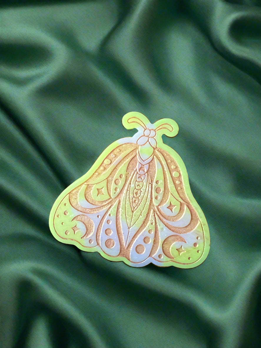 A Luna Moth wax melt with intricate patterns, placed on a green textured surface.