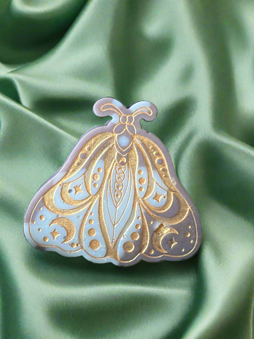 A Luna Moth wax melt with intricate patterns, placed on a green textured surface.