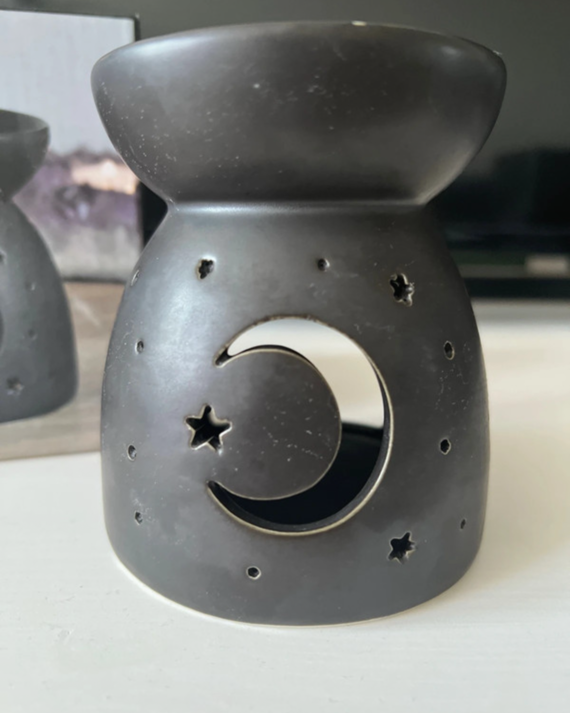 Black ceramic oil burner with moon and star design on a white surface.