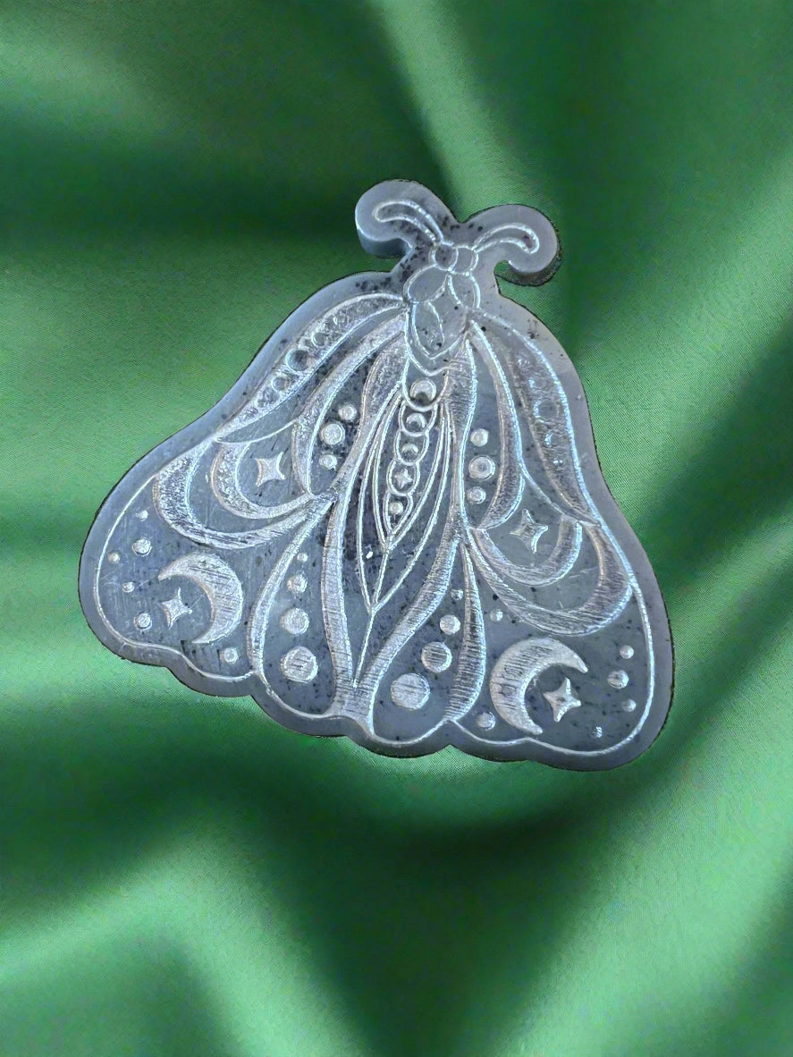 A Luna Moth wax melt with intricate patterns, placed on a green textured surface.
