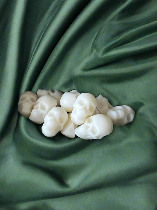 A pile of white, skull-shaped wax melts placed on a dark green fabric backdrop.