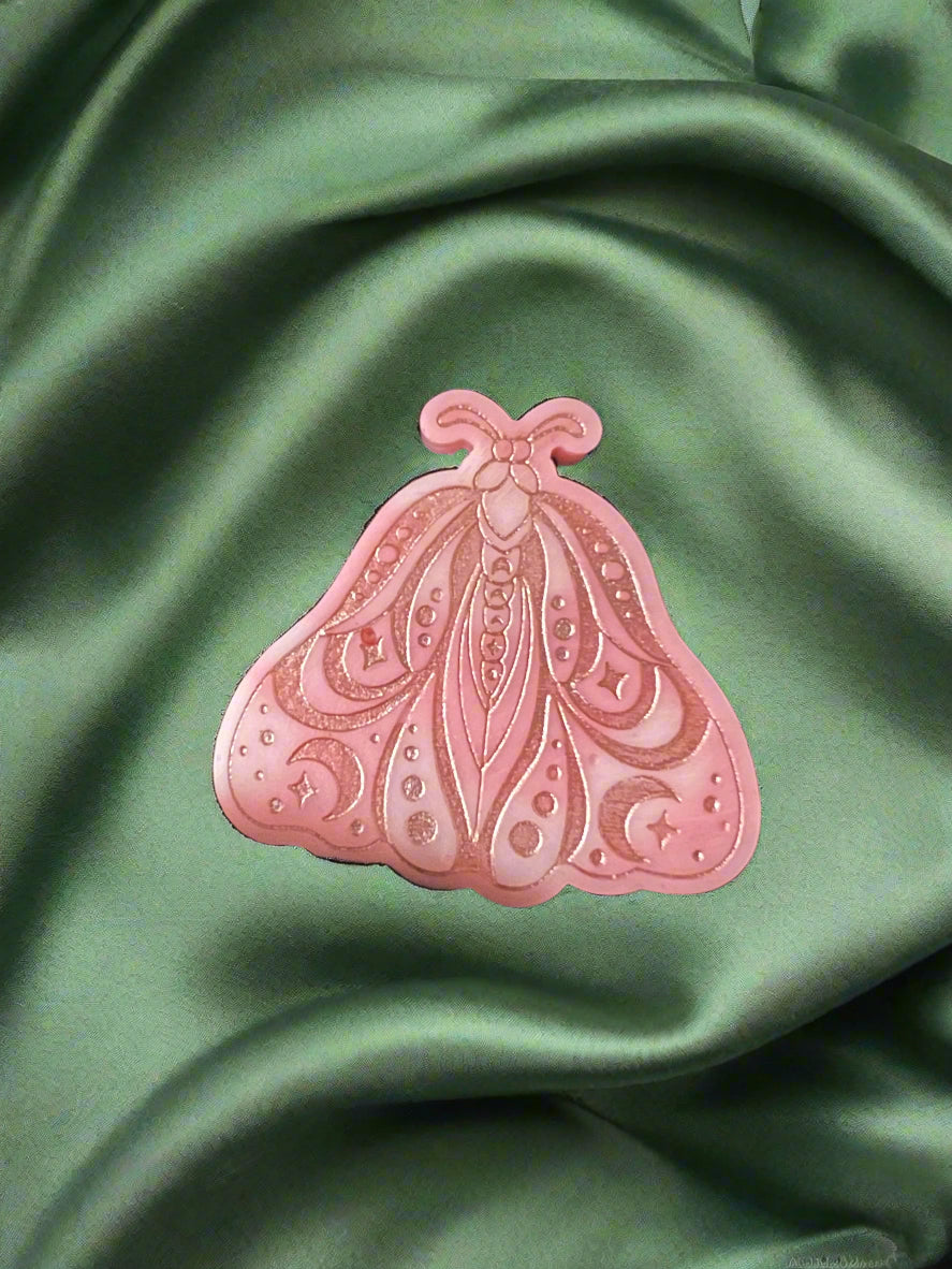 A Luna Moth wax melt with intricate patterns, placed on a green textured surface.