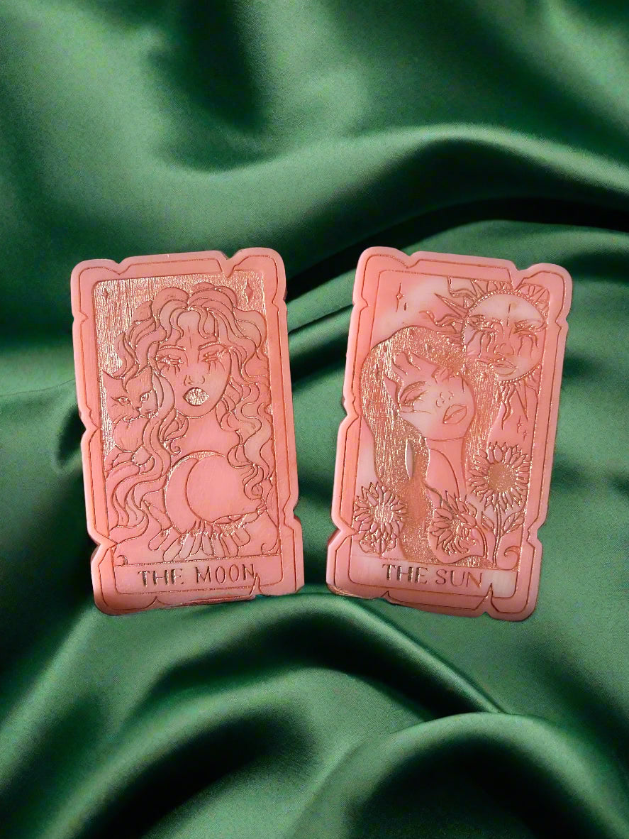 Two tarot card-shaped wax melts, one labeled 'THE SUN' and the other 'THE MOON', placed on a green fabric surface.