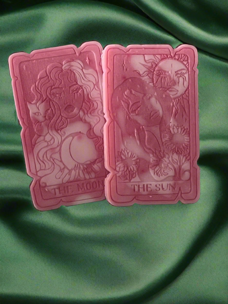 Two tarot card-shaped wax melts, one labeled 'THE SUN' and the other 'THE MOON', placed on a green fabric surface.