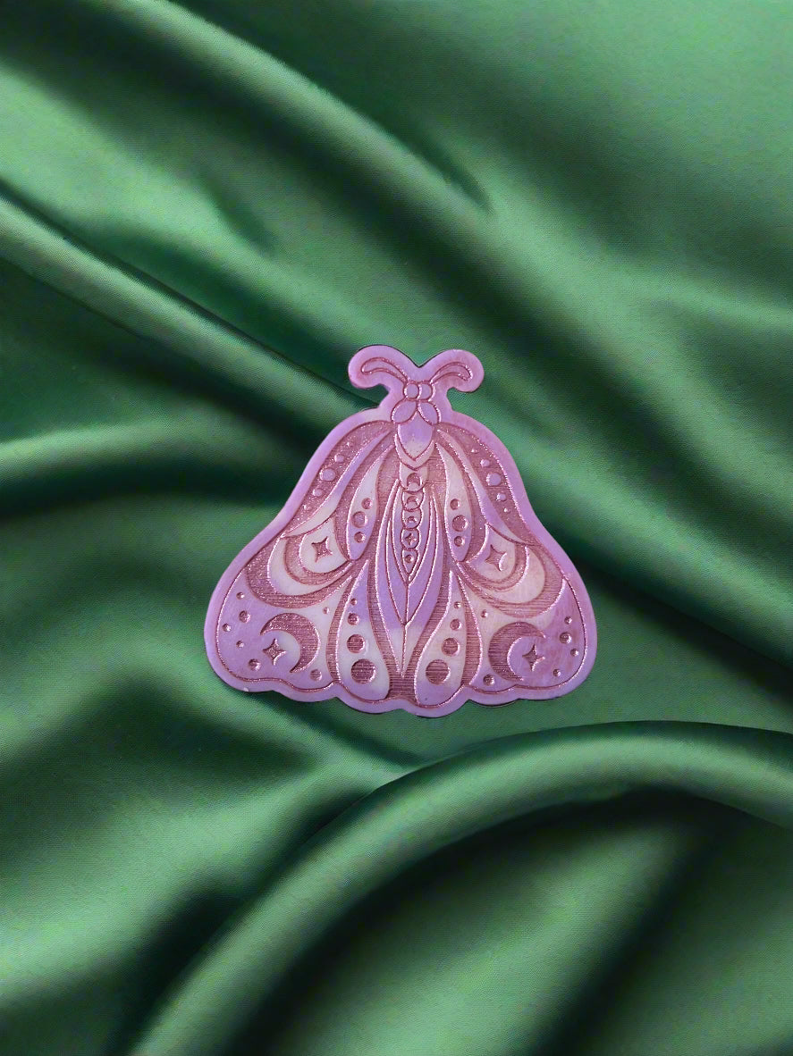 A Luna Moth wax melt with intricate patterns, placed on a green textured surface.