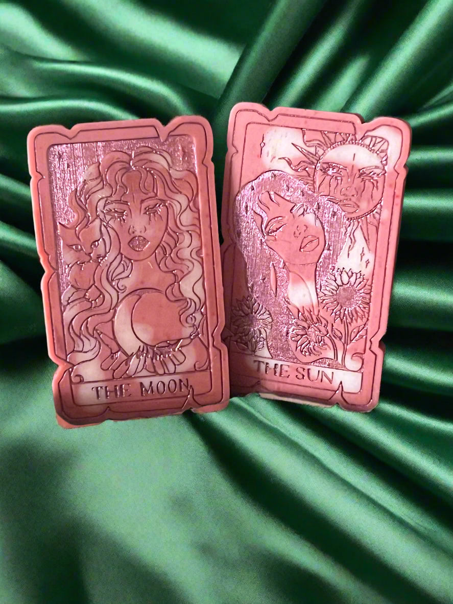 Two tarot card-shaped wax melts, one labeled 'THE SUN' and the other 'THE MOON', placed on a green fabric surface.