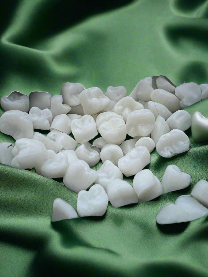 A collection of white wax melts shaped like teeth, placed on a dark green fabric surface.
