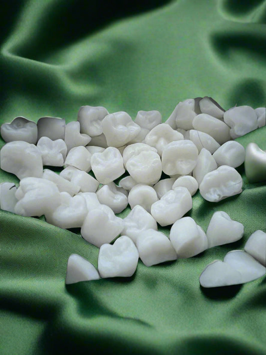 A collection of white wax melts shaped like teeth, placed on a dark green fabric surface.